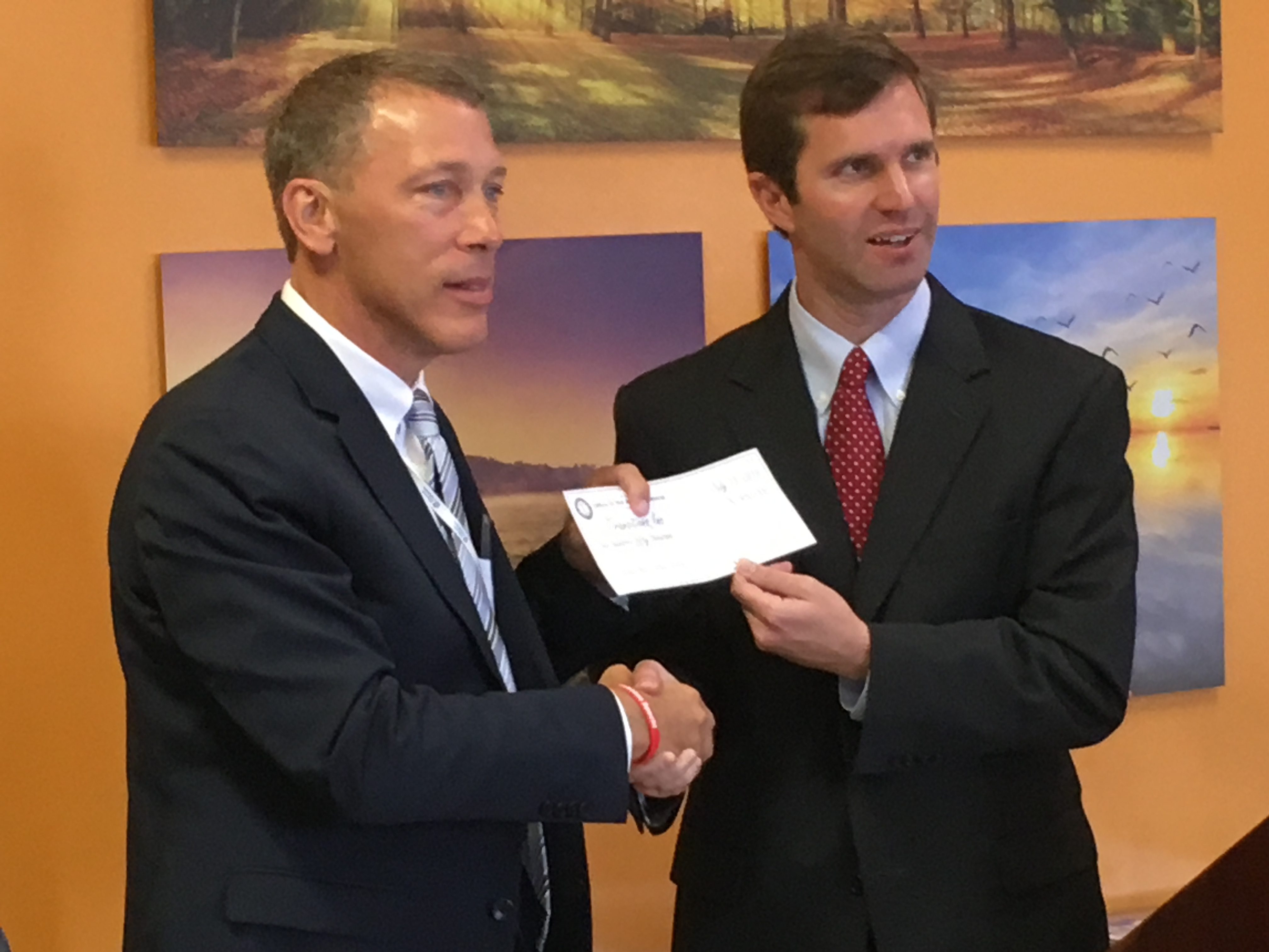 Jim Beiting, executive director of Transitions Inc. (left), accepts a check for $450,000 from Attorney General Andy Beshear. The funds will be used to support Transitions' WRAP House in Covington.
