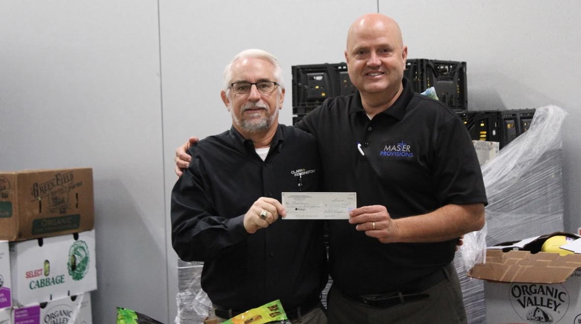 Bill Winegardner, at left, presents a check to Roger Babik. The two are in Master Provisions' cold storage unit, among the fresh fruits and vegetables the organization provides to agencies that feed the hungry.